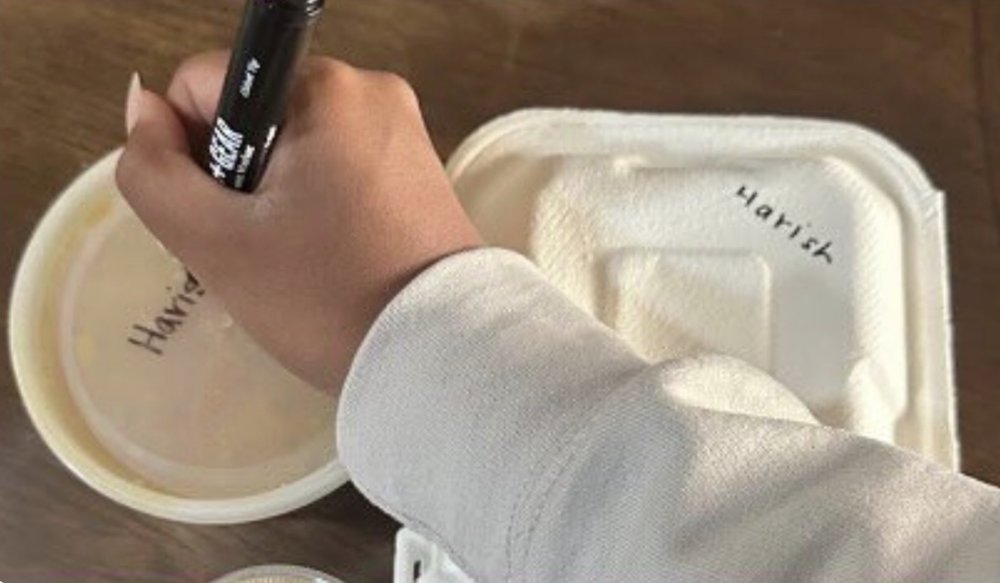 A hand writing a name on a food container with a marker