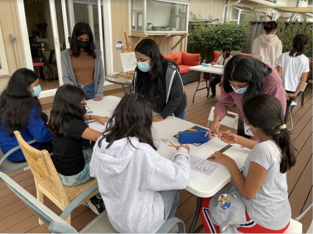 Students and CARES members drawing together at a table on a sunny patio
