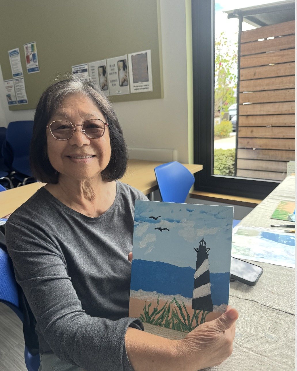 A participant in glasses holding up her lighthouse painting