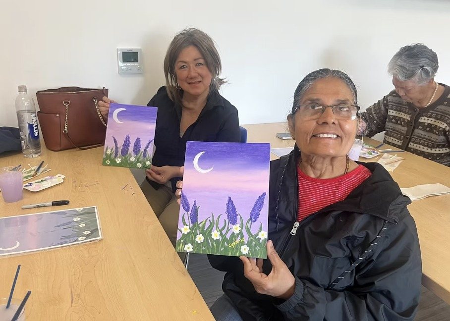 Two women proudly holding up their moon and lavender paintings