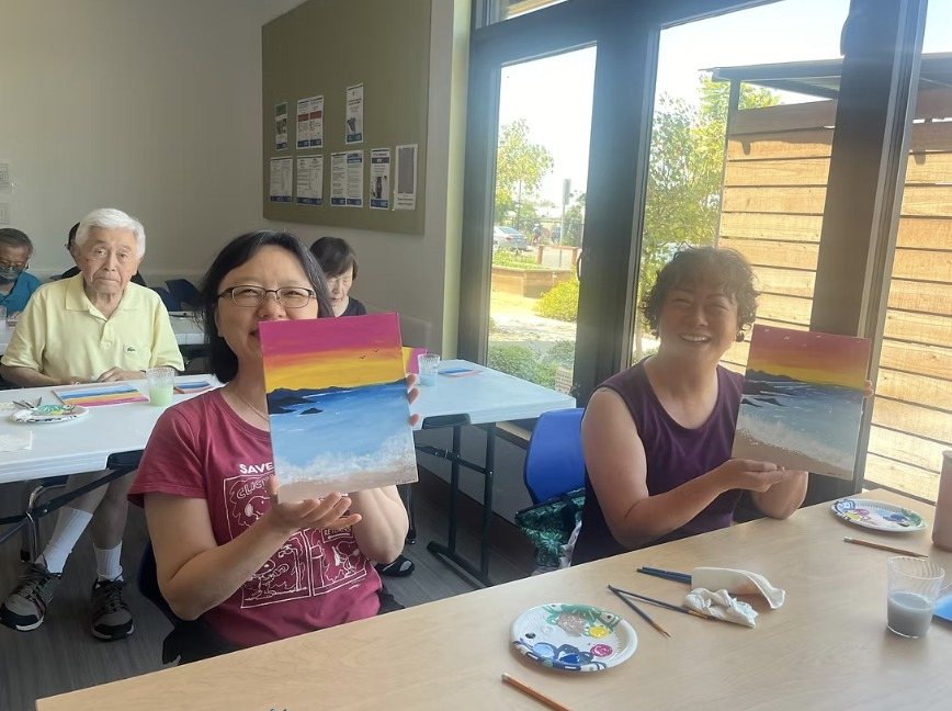 Participants smiling and holding up their sunset paintings
