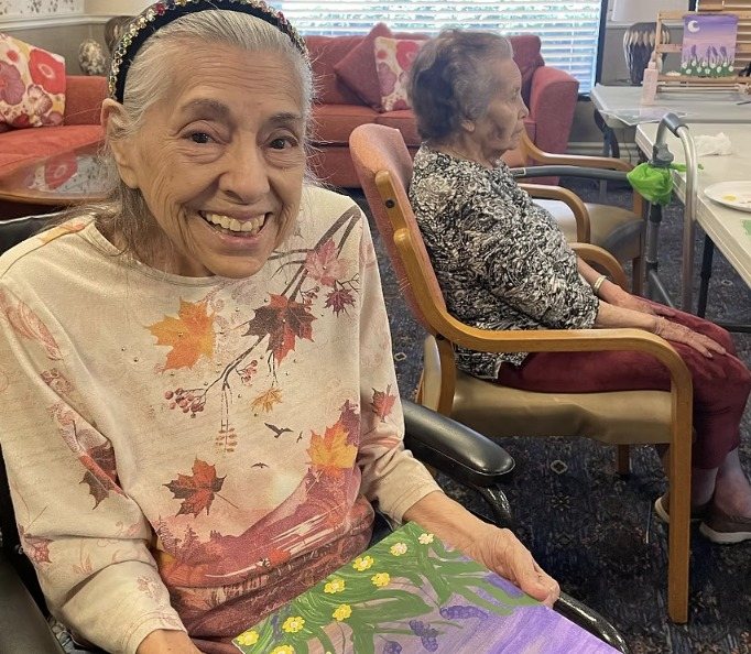 A smiling resident holding her painting in the lounge at Berg Communities