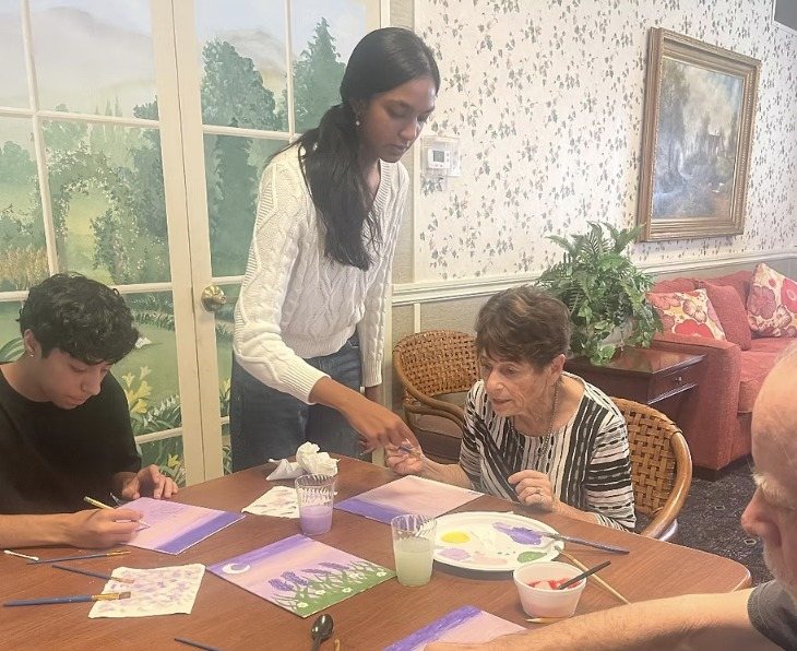 A CARES officer helping residents paint lavender moon paintings at a round table