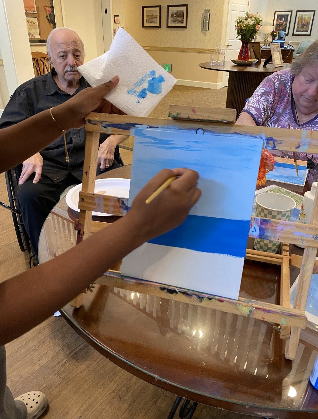 A CARES volunteer helping a participant paint the ocean on an easel