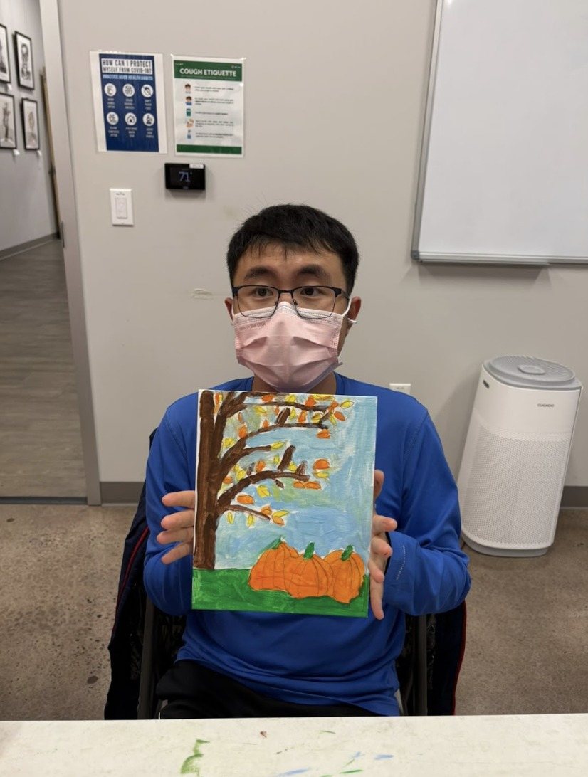 A participant holding up his autumn tree painting with orange pumpkins