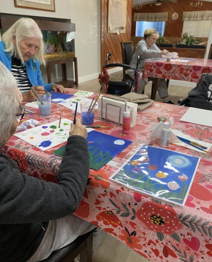 Residents painting at a table with a red floral tablecloth