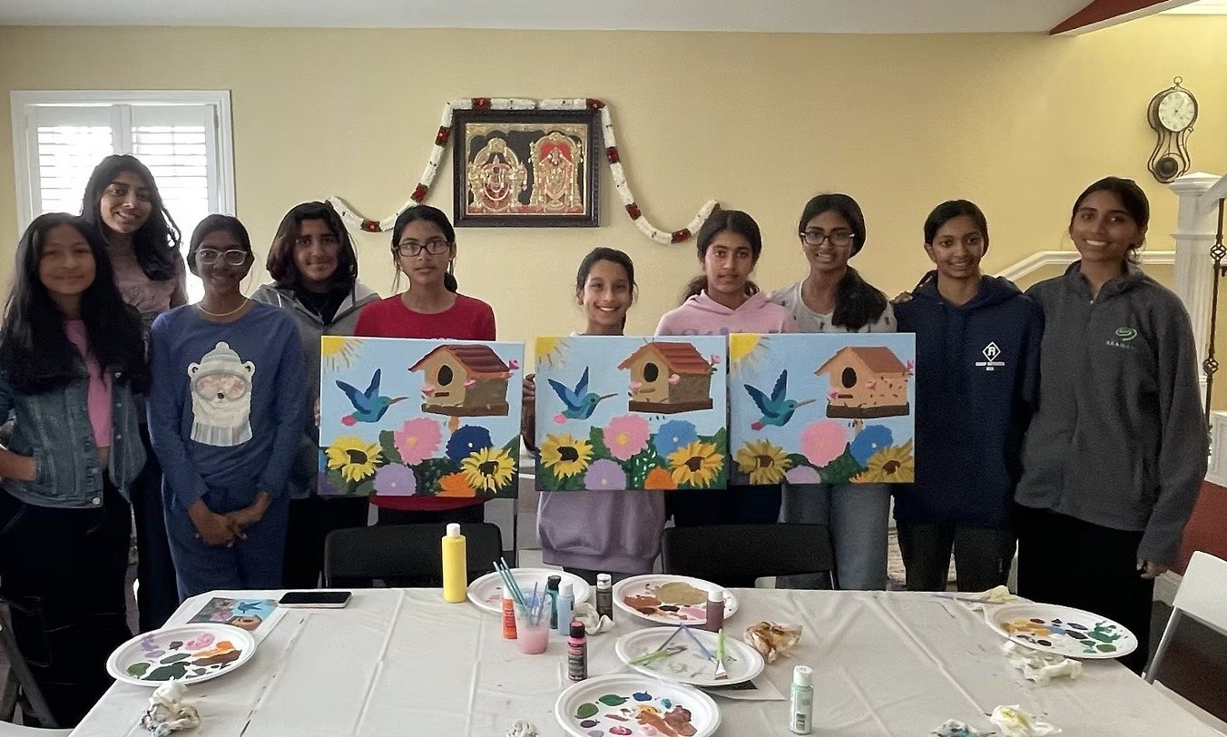 A troop standing behind three finished paintings of a hummingbird, a birdhouse, and flowers