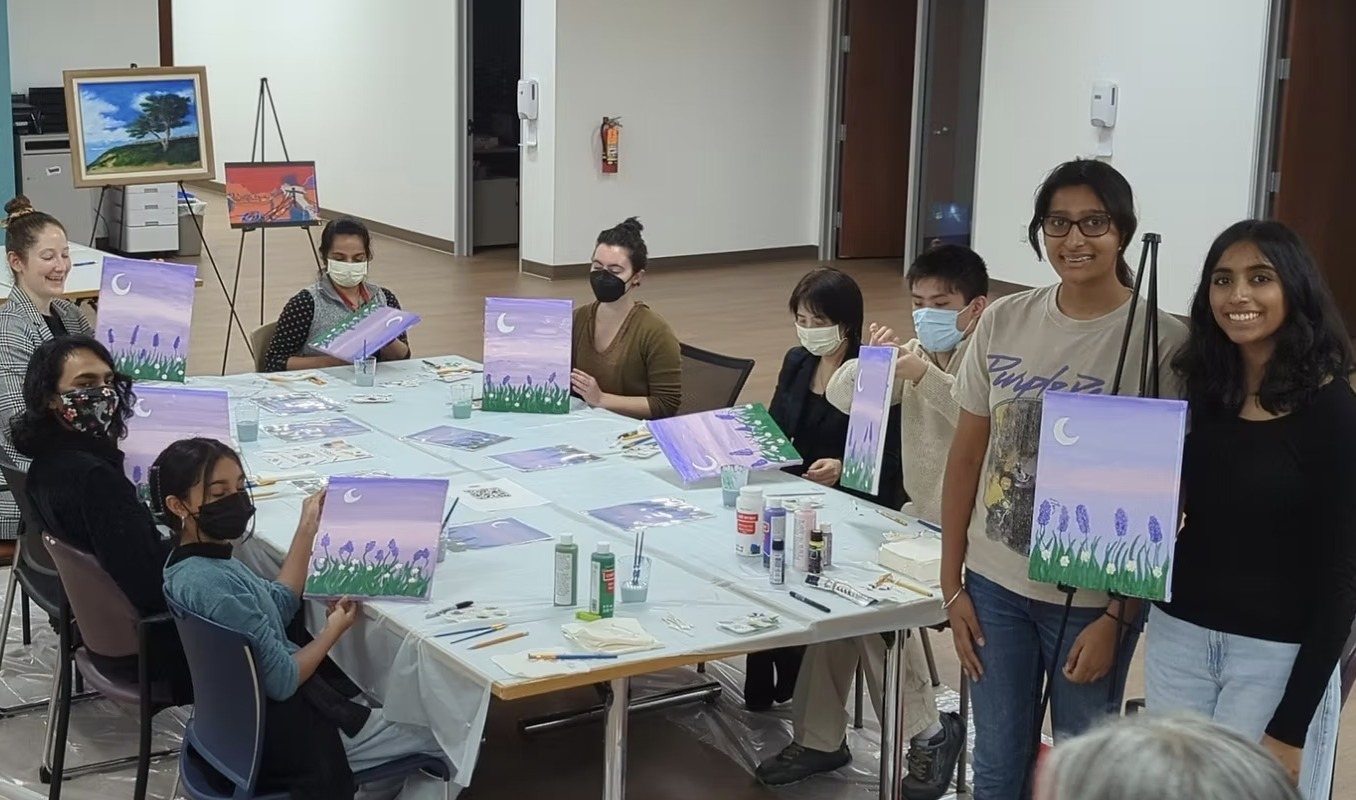 Participants and CARES officers holding up their lavender moon paintings at a long table